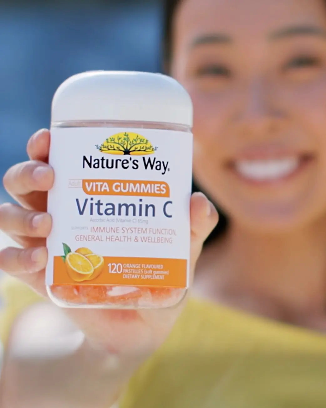 Person holding a container of Nature's Way Vitamin C gummies with a blurred background.