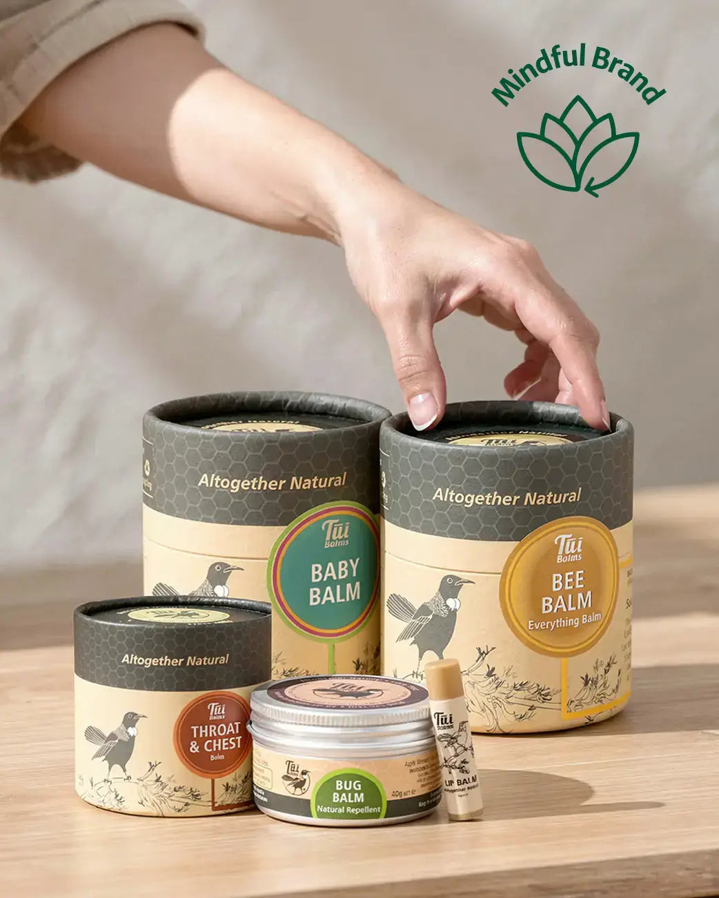 Hand reaching for a container of 'Altogether Natural' balm on a wooden surface with the brand logo visible.