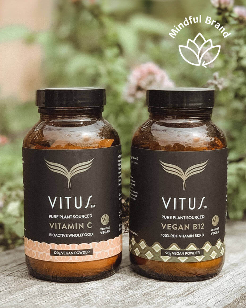 Two bottles of Vitus vitamin products on a wooden surface with a blurred natural background.