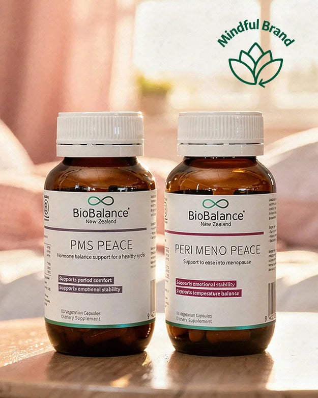 BioBalance PMS Peace and Per Meno Pause on a wooden surface with a neutral pink bed and window in a softly diffused and blurred background.