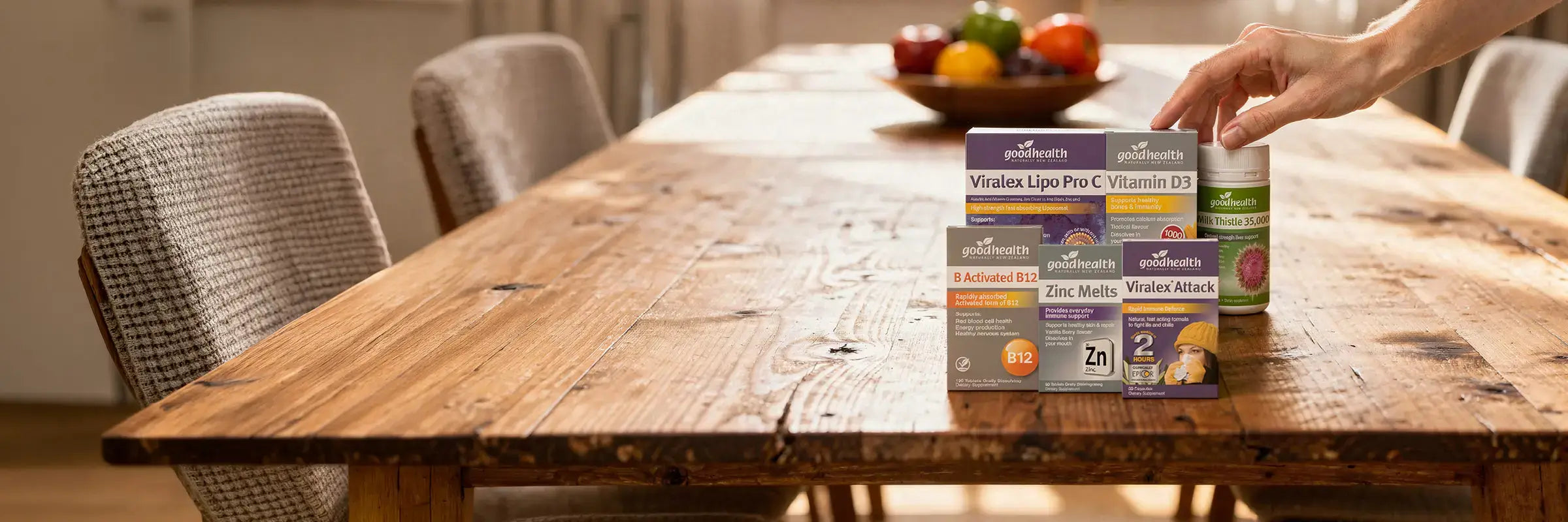 Hand picking Good Health supplement products from a wooden table.