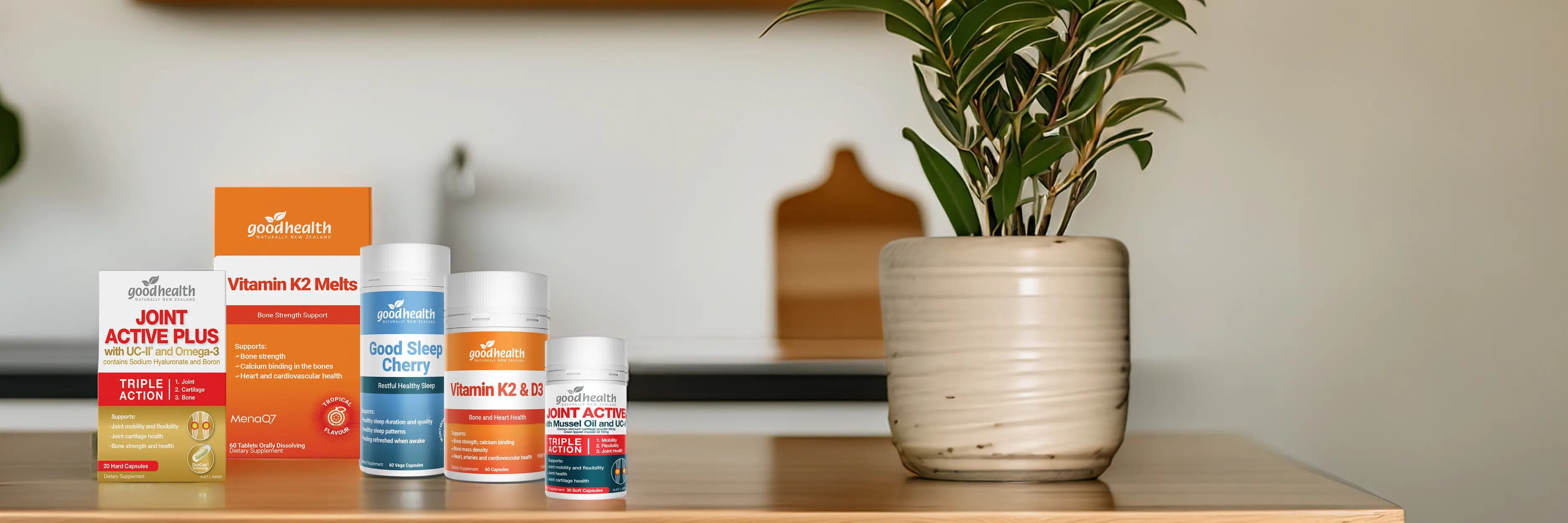 Collection of Good Health supplement products on a wooden surface next to a plant.