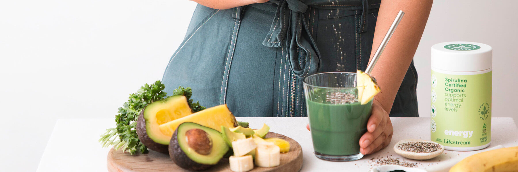 Person making spirulina on a white counter with fresh fruit and vegetables.
