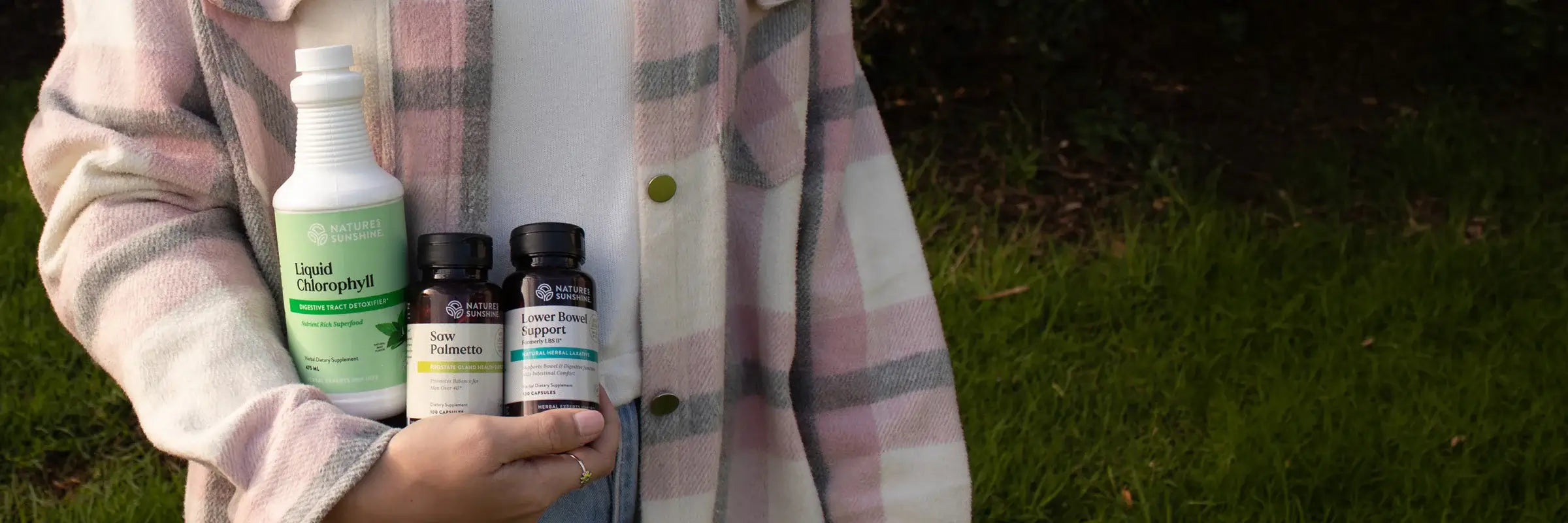 Person wearing a pink jacket holding supplement products outside.