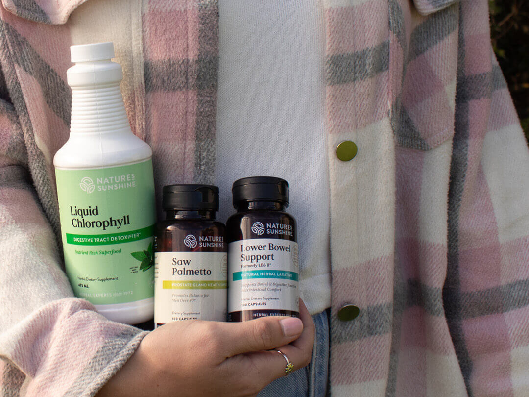 Person wearing a pink jacket holding supplement products outside.