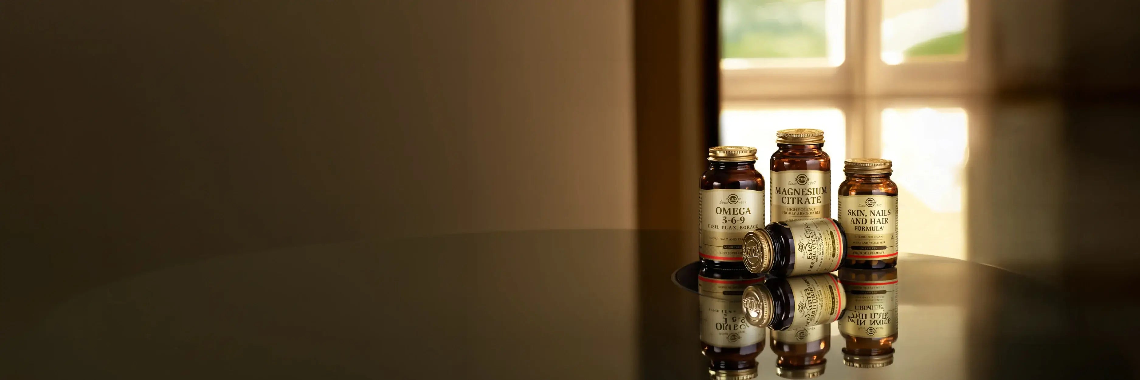 Four amber glass supplement bottles with gold caps in a dimly lit room near a window.