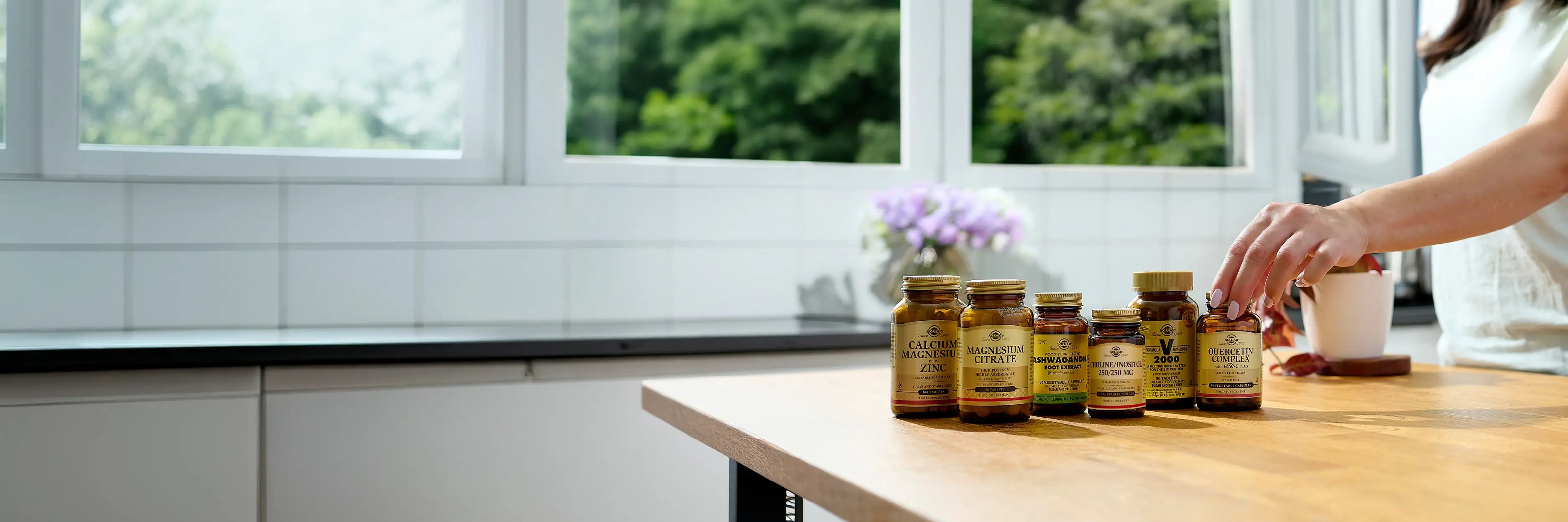 Row of supplement bottles on a kitchen counter with a window in the background