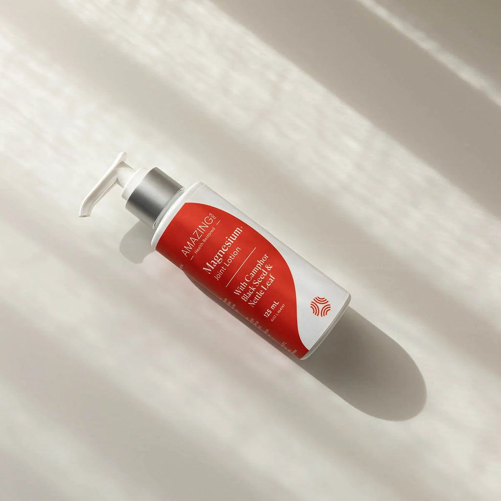 Amazing Oils Magnesium Joint Lotion with Camphor Black Seed & Nettle Leaf on a white surface with dappled light.