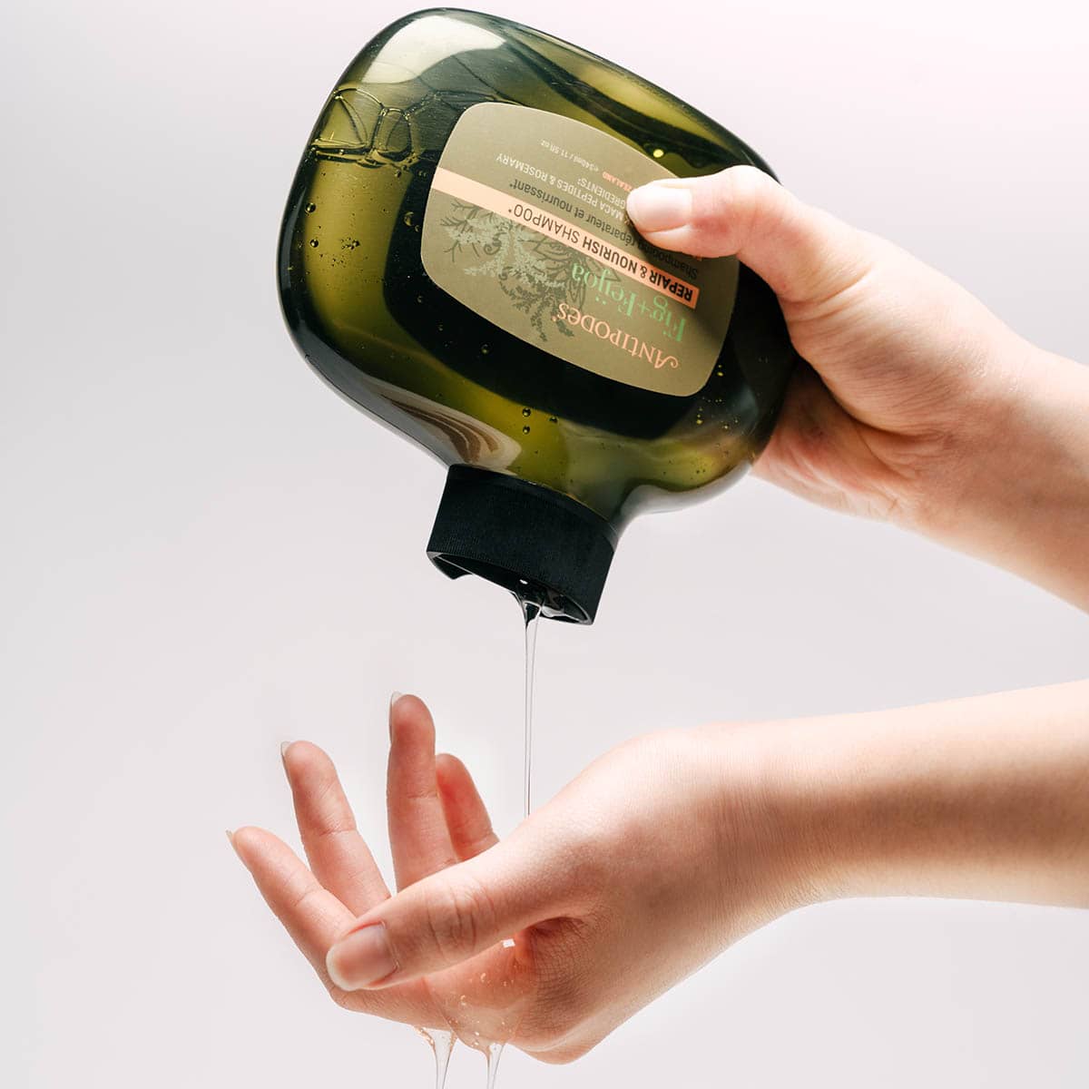Hand using a soap dispenser to apply liquid soap to another hand against a light background.