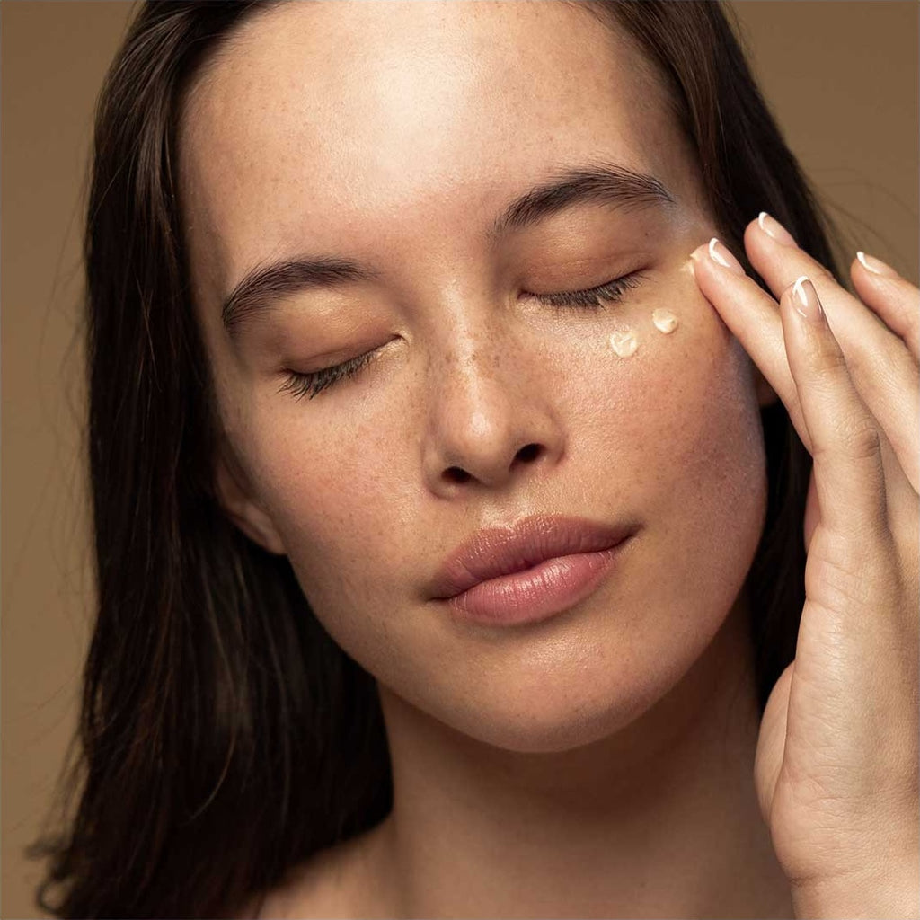 Woman applying cream to her face with a neutral background