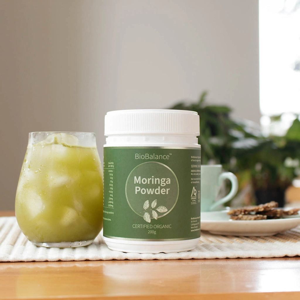BioBalance Moringa Powder container with a glass of green iced moringa drink on a table.