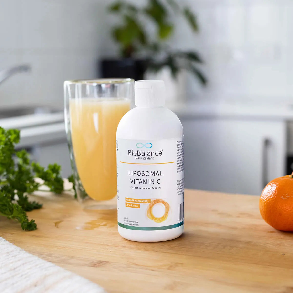 BioBalance liposomal vitamin C bottle on a wooden table with a glass of juice and an orange.