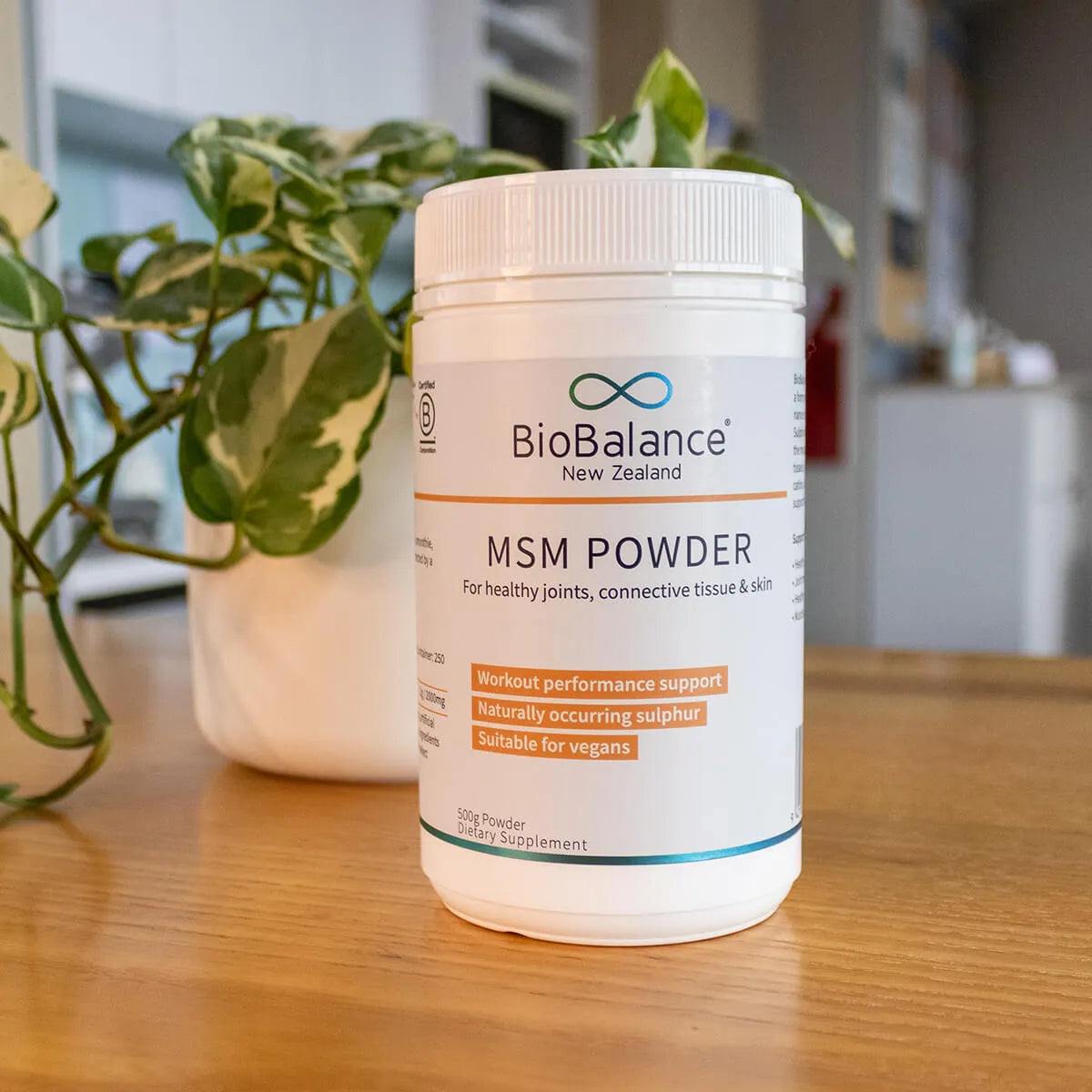 BioBalance MSM Powder container on a wooden surface with plants in the background.