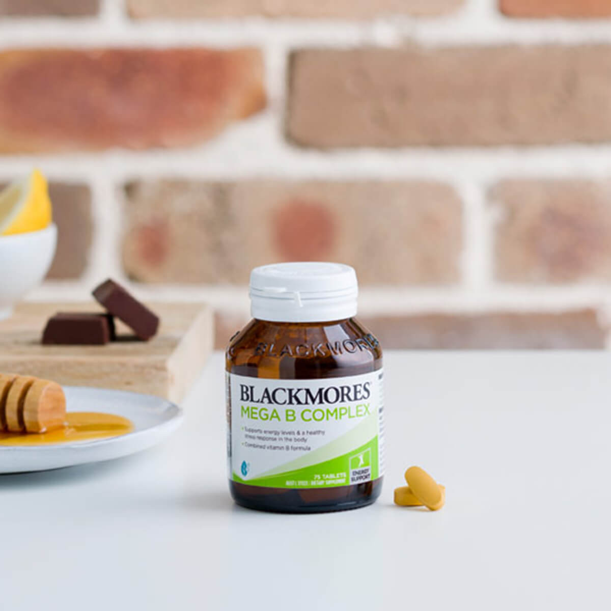 Blackmores Mega B Complex supplement bottle on a table with a brick wall background.