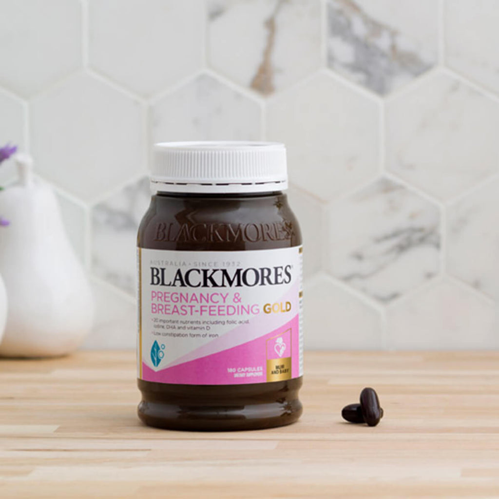 Blackmores Pregnancy & Breast-Feeding Gold supplement bottle on a wooden surface with a tiled wall background.