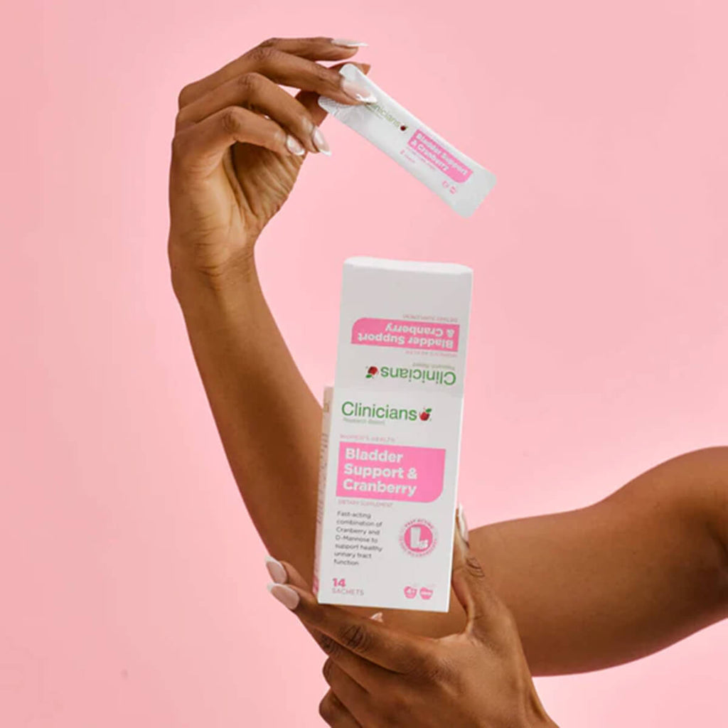 Hand holding Clinicians Bladder Support & Cranberry product against a pink background.