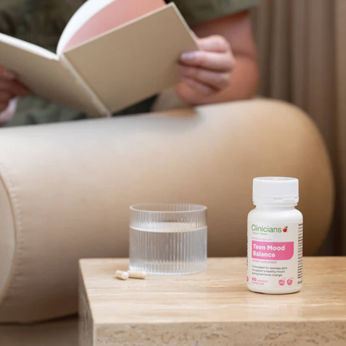 CliniCana Teen Mood Balance supplement bottle on a table with a glass of water and a book in the background.
