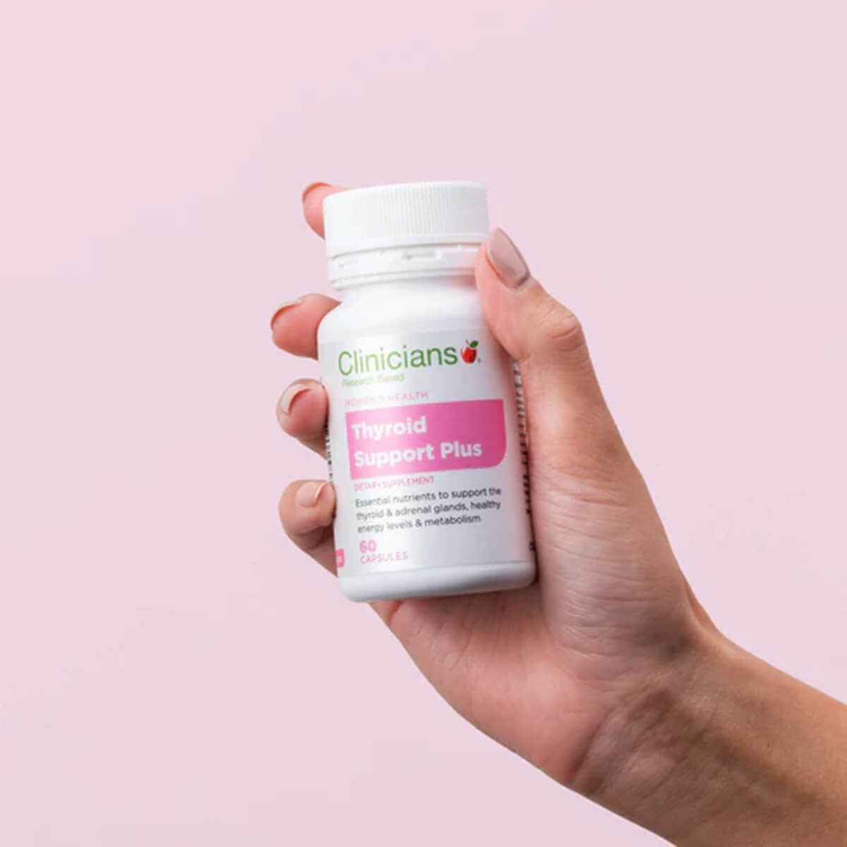 Hand holding a bottle of 'Clinicians Thyroid Support Plus' against a pink background.