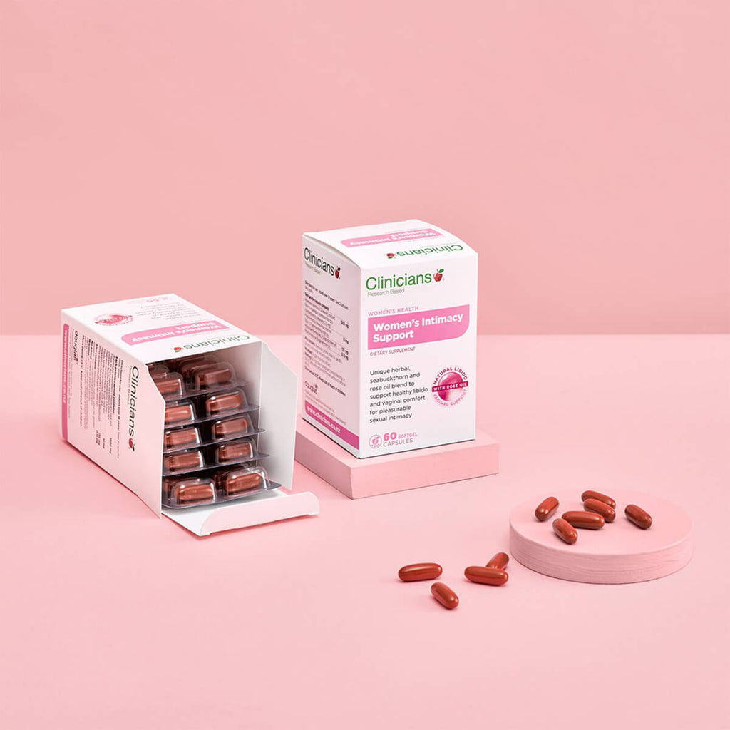 Box of supplements and red pills on a pink surface.