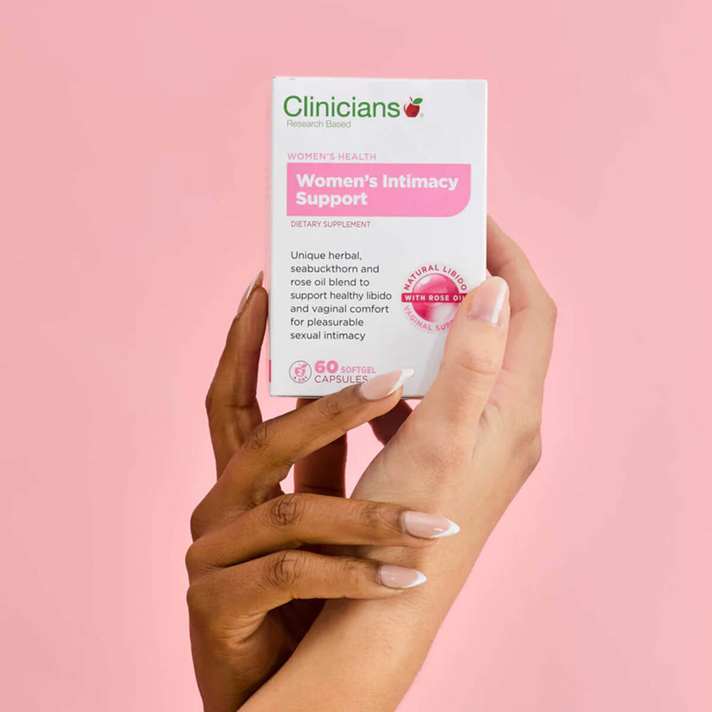 Hand holding box of supplements against a pink background.