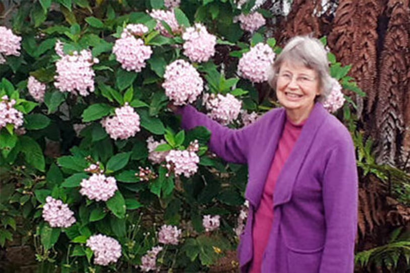 woman in purple cardigan standing proudly in front of pink hydrangeas