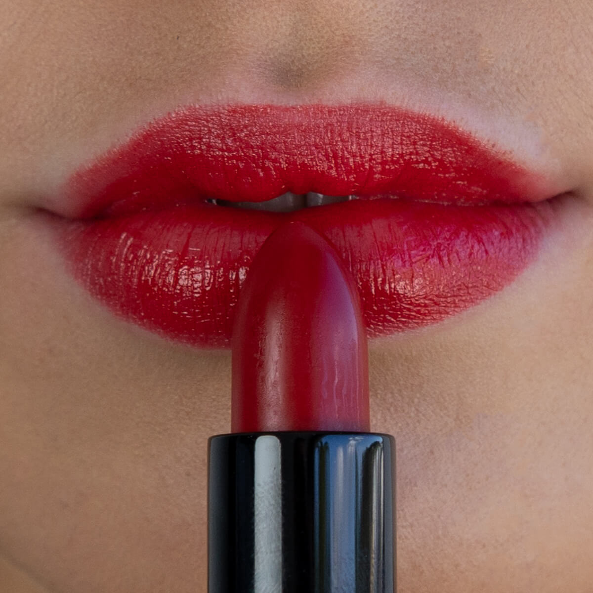 Close-up of a person applying red lipstick to their lips.