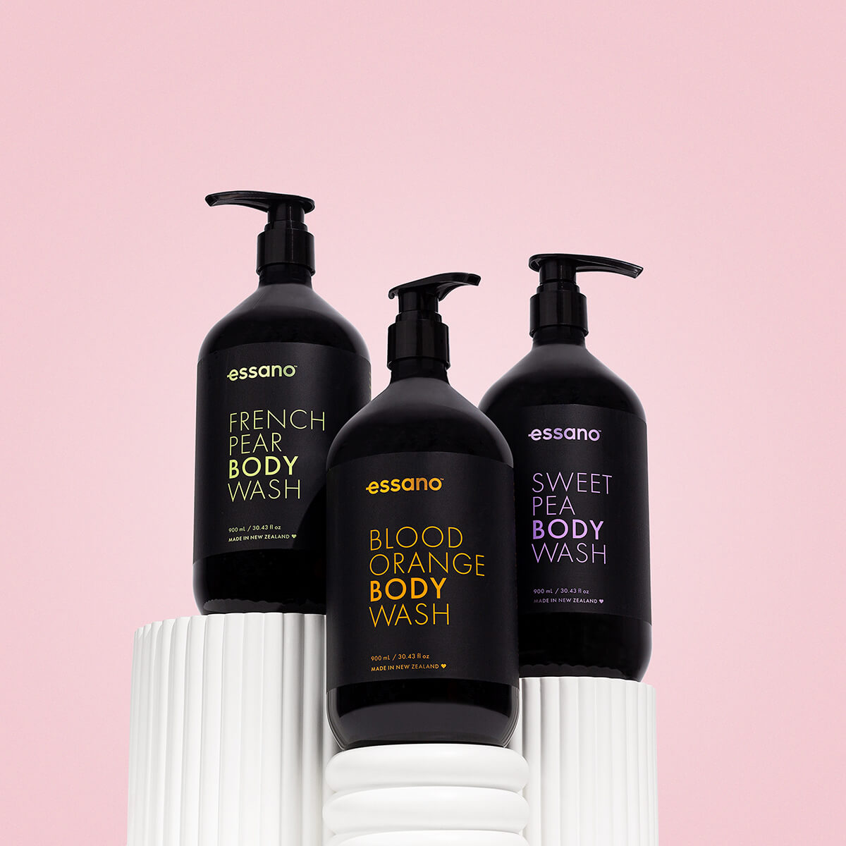 Three black body wash bottles with pump dispensers on a pink background.
