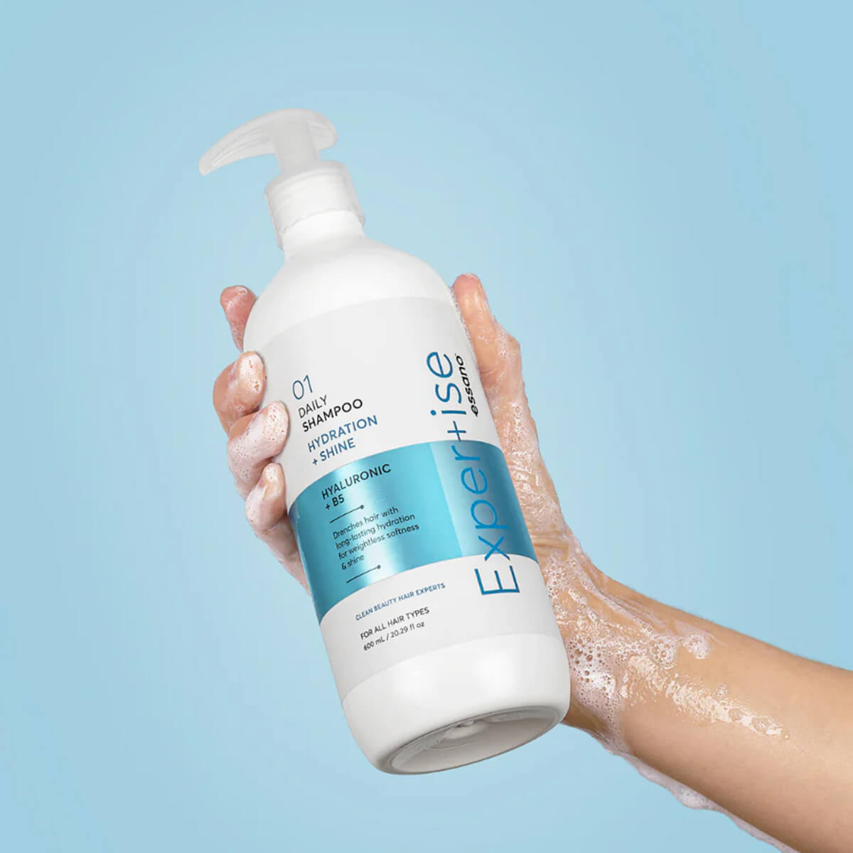 Hand holding a bottle of 'Expertise' shampoo against a light blue background.