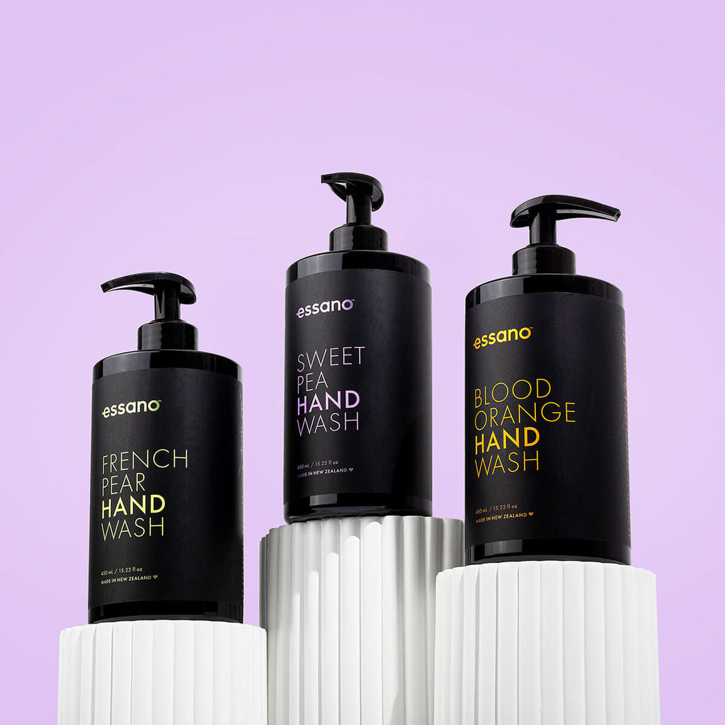 Three bottles of Essano hand wash on a white pedestal against a purple background.