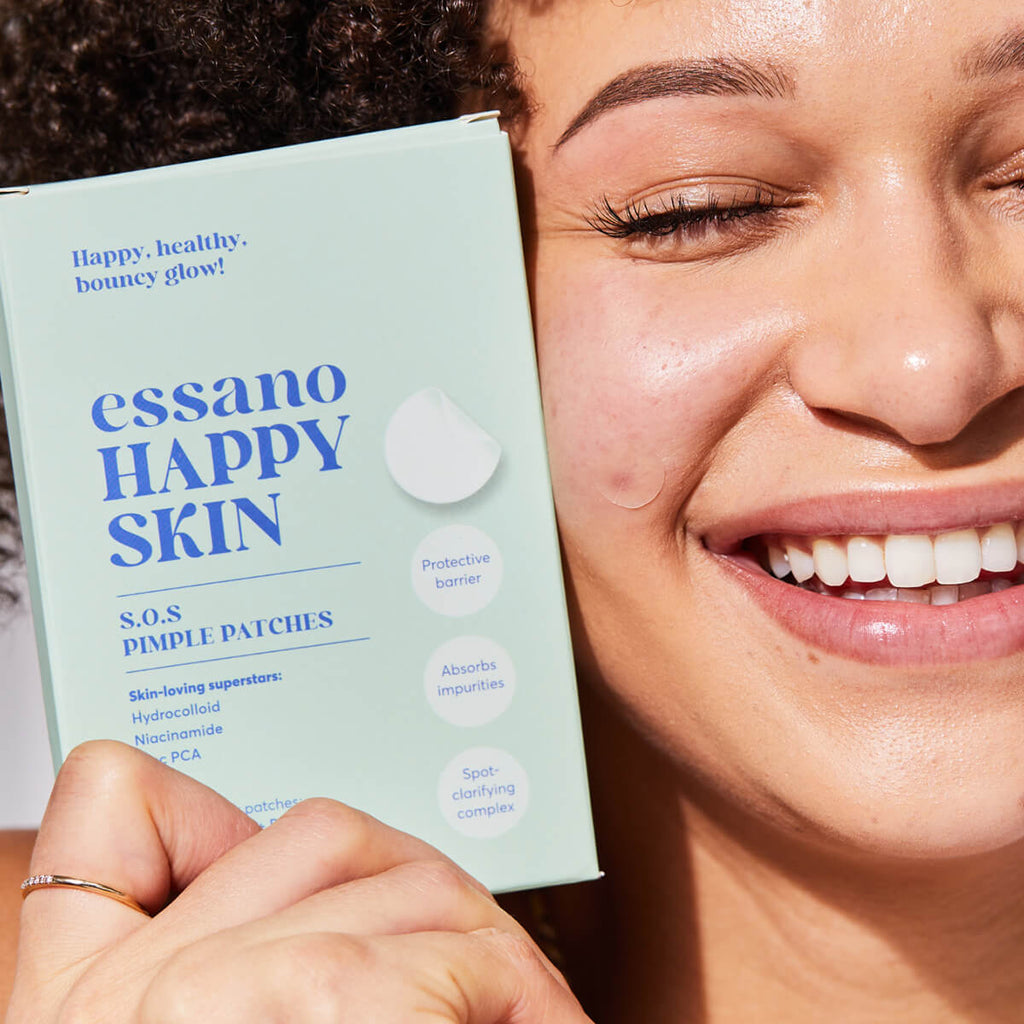 Person holding a box of essano Happy Skin pimple patches with a close-up of their face.