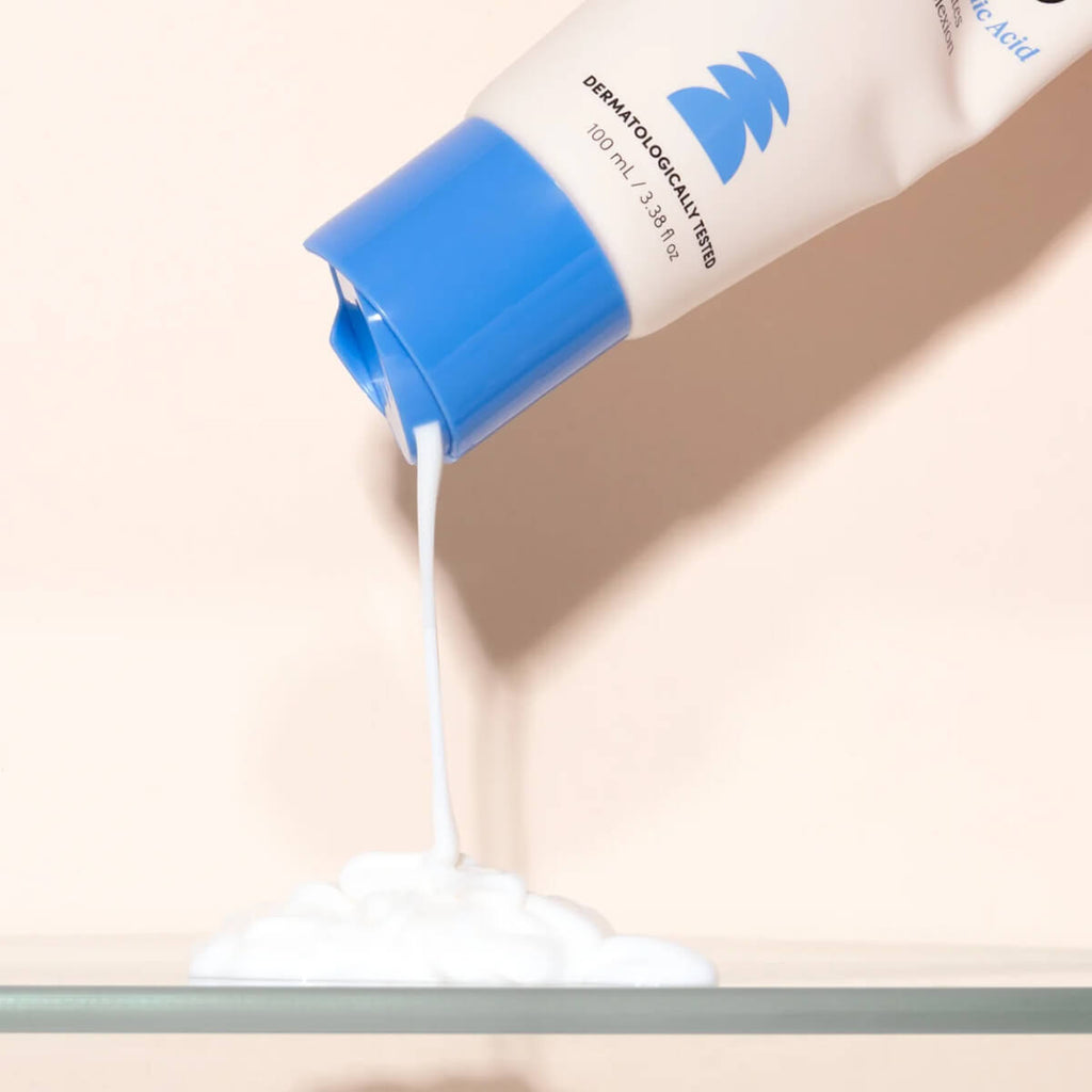 Tube of cream with blue cap and white body on a beige background.