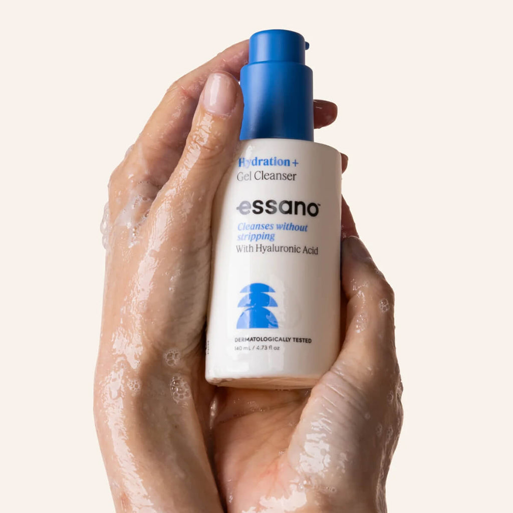 Hand holding a bottle of essano Hydration+ Gel Cleanser with a beige background.