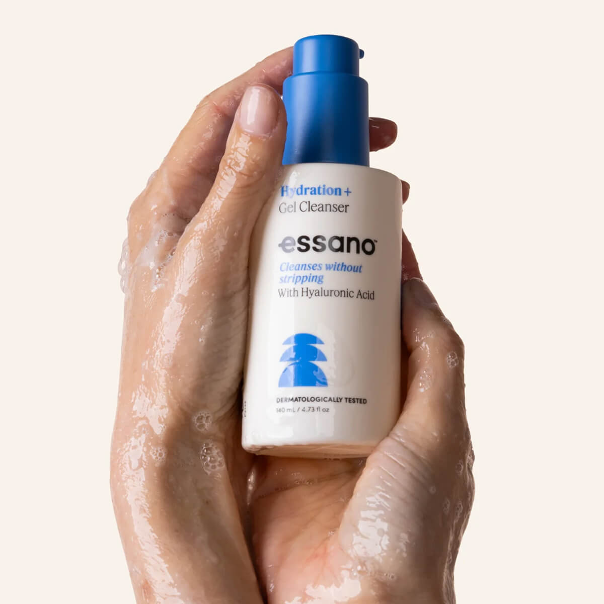 Hand holding a bottle of essano Hydration+ Gel Cleanser with a beige background.