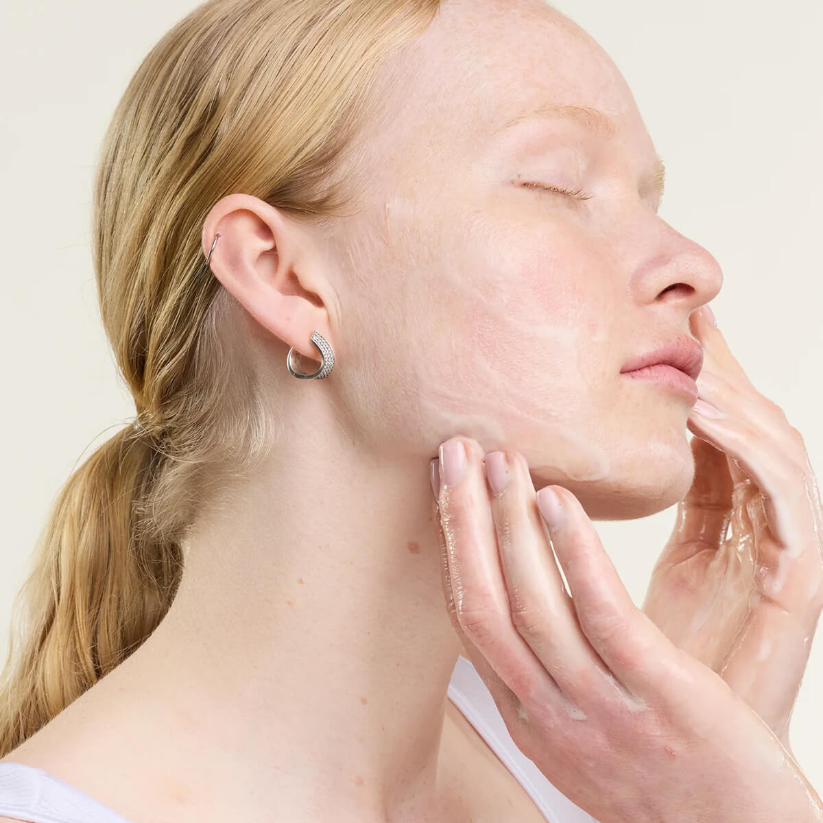 Woman touching her face with a neutral background.