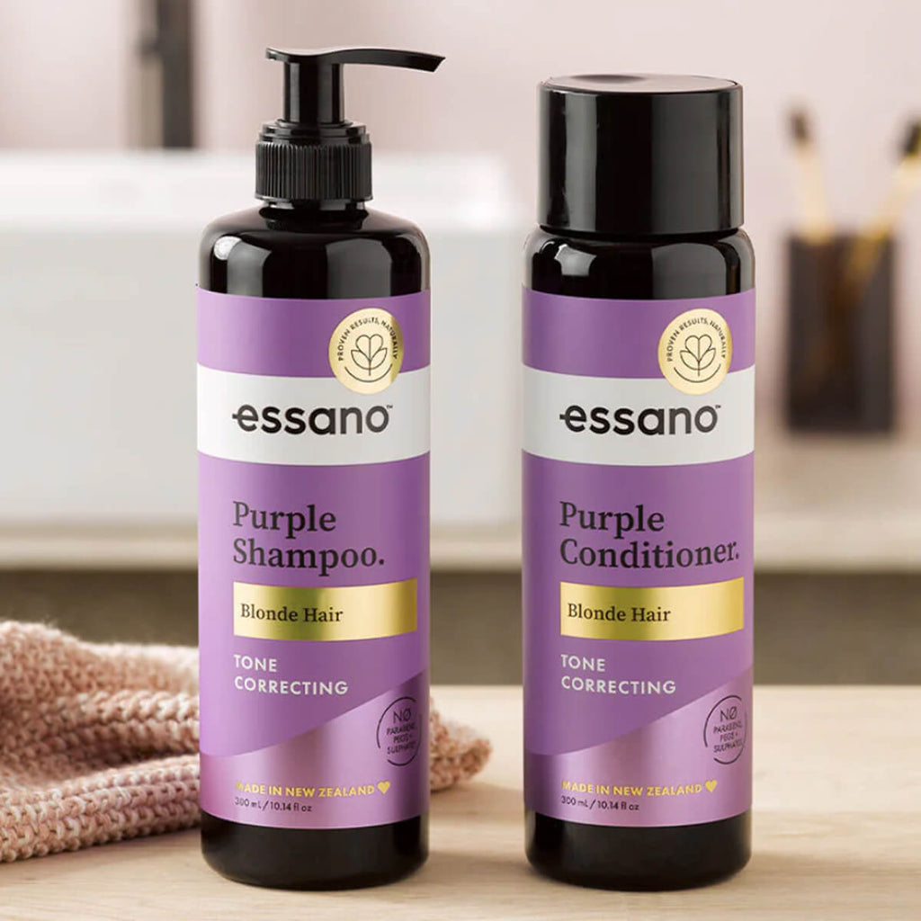 Two bottles of essano Purple Shampoo and Conditioner on a wooden surface with a blurred background.