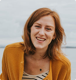 Woman with red hair in a mustard coloured cardigan smiling at the beach