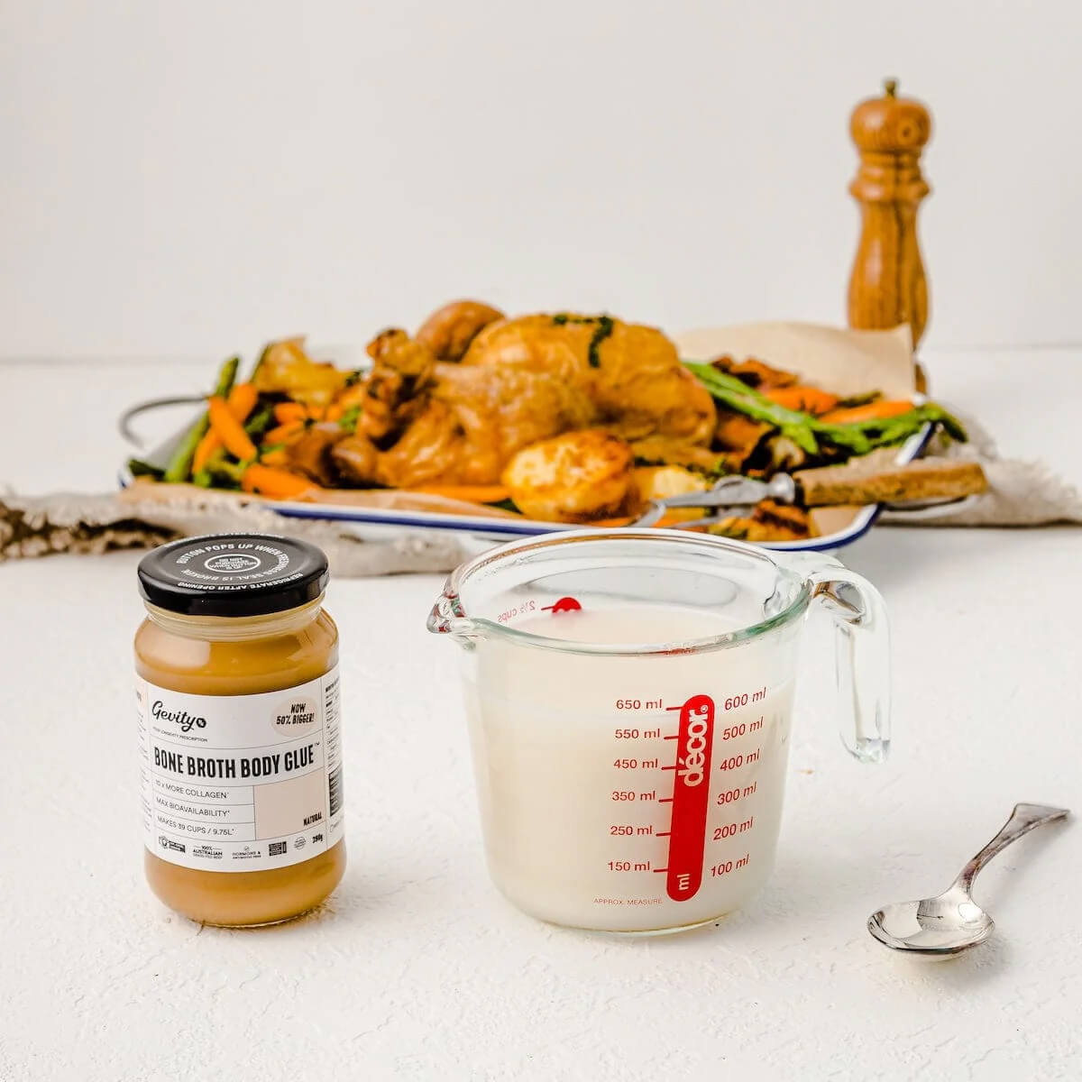 Jar of Bone Broth Body Glue and measuring cup with liquid on a table with food in the background.