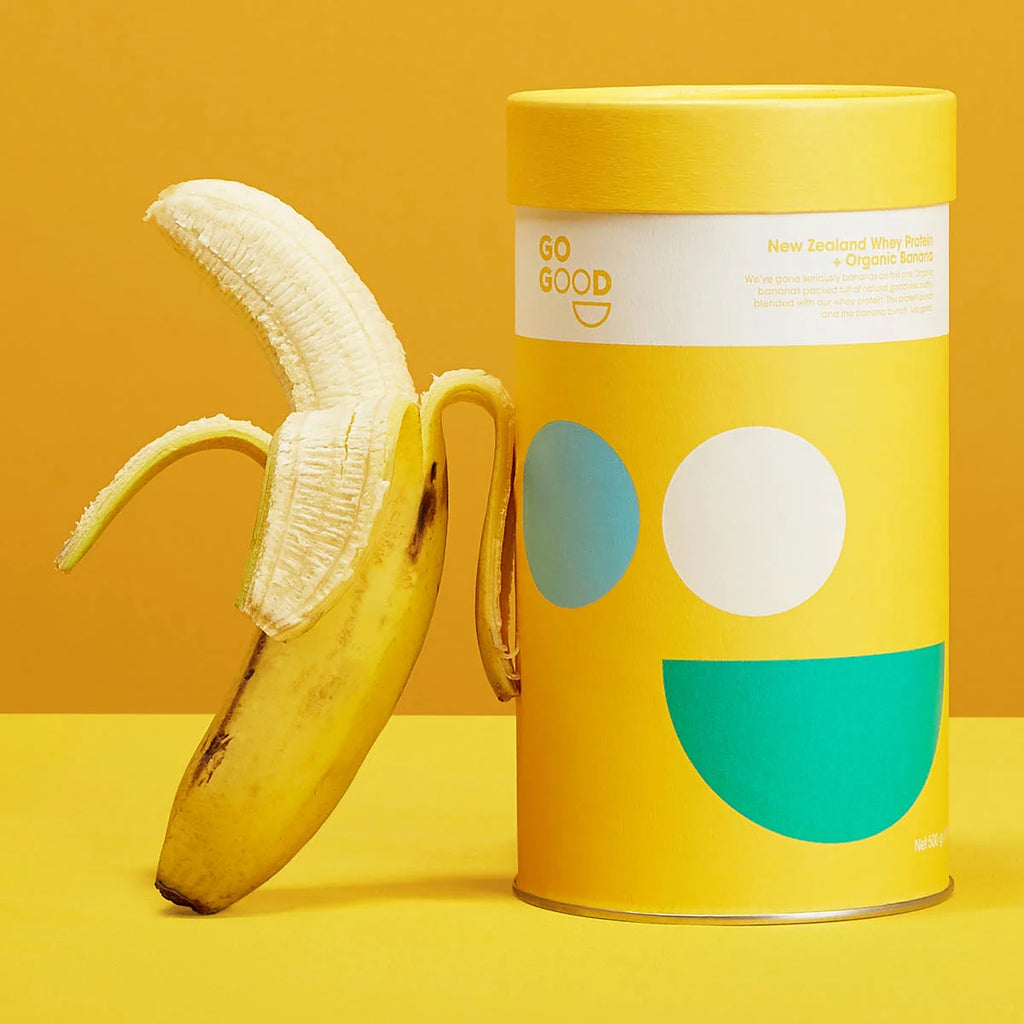 Yellow banana next to whey protein cylindrical container with geometric designs on a yellow background