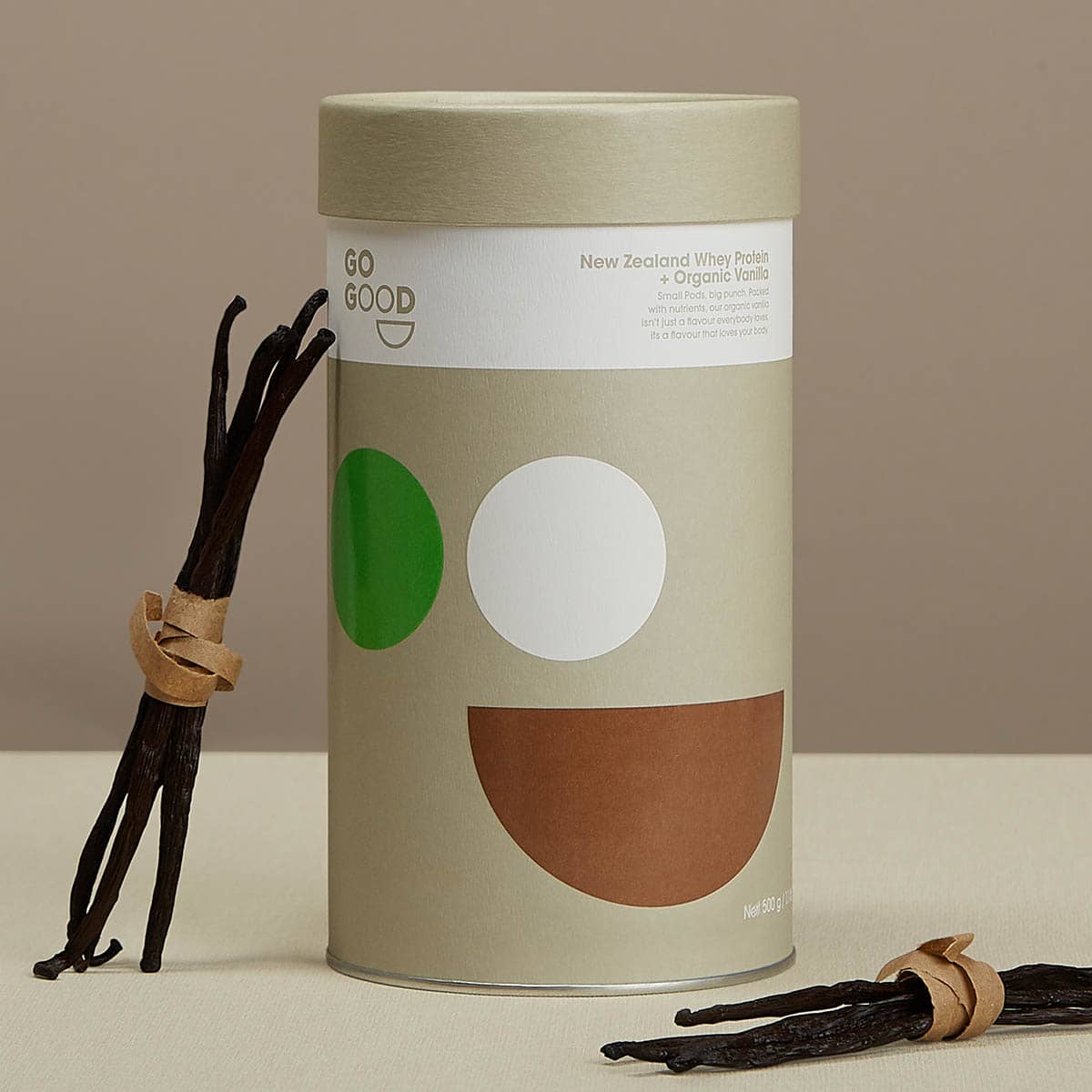 Vanilla beans next to a cylindrical container with 'GO GOOD' branding on a beige background.