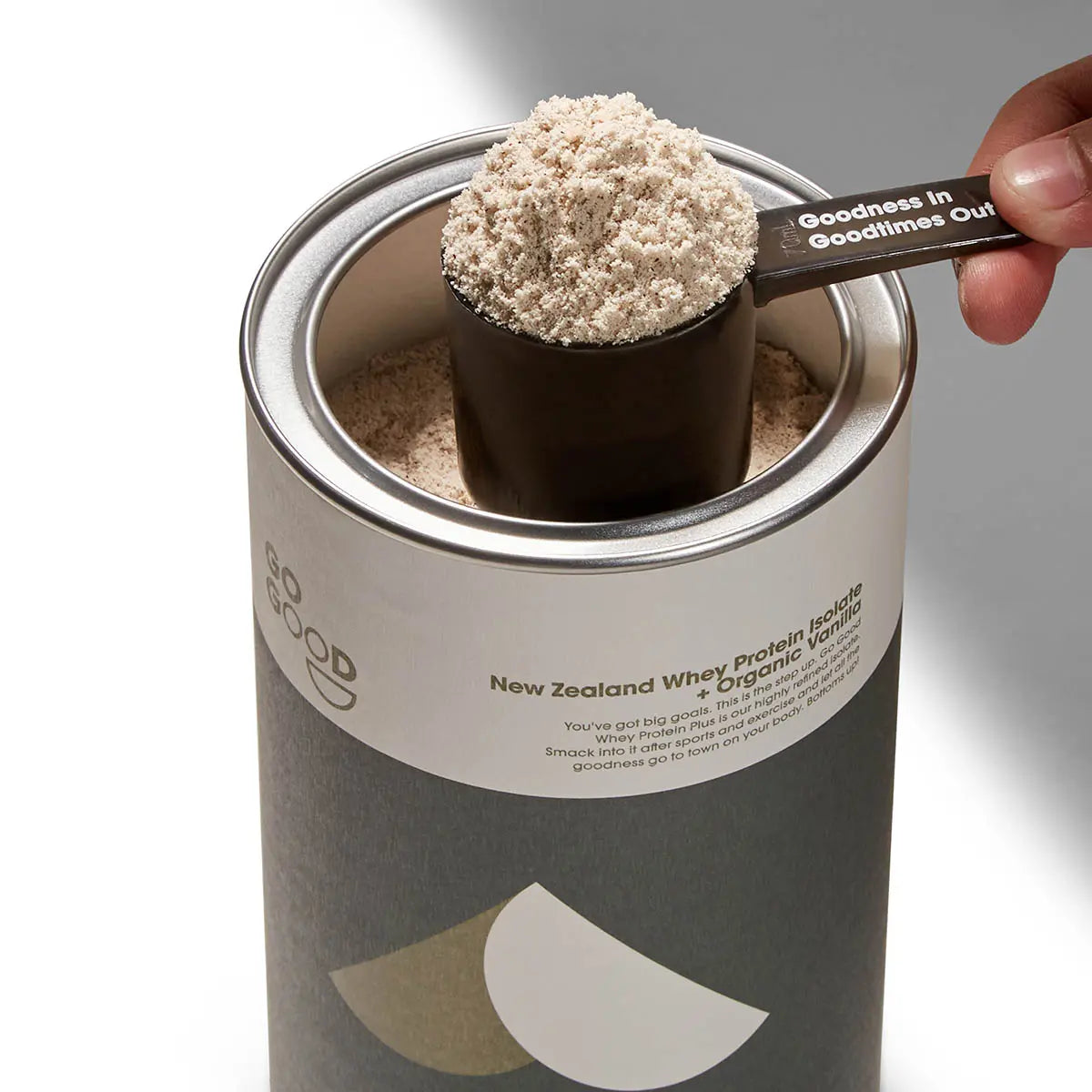 Protein powder scoop being taken from a container labeled 'New Zealand Whey Protein Isolate + Organic Vanilla'.