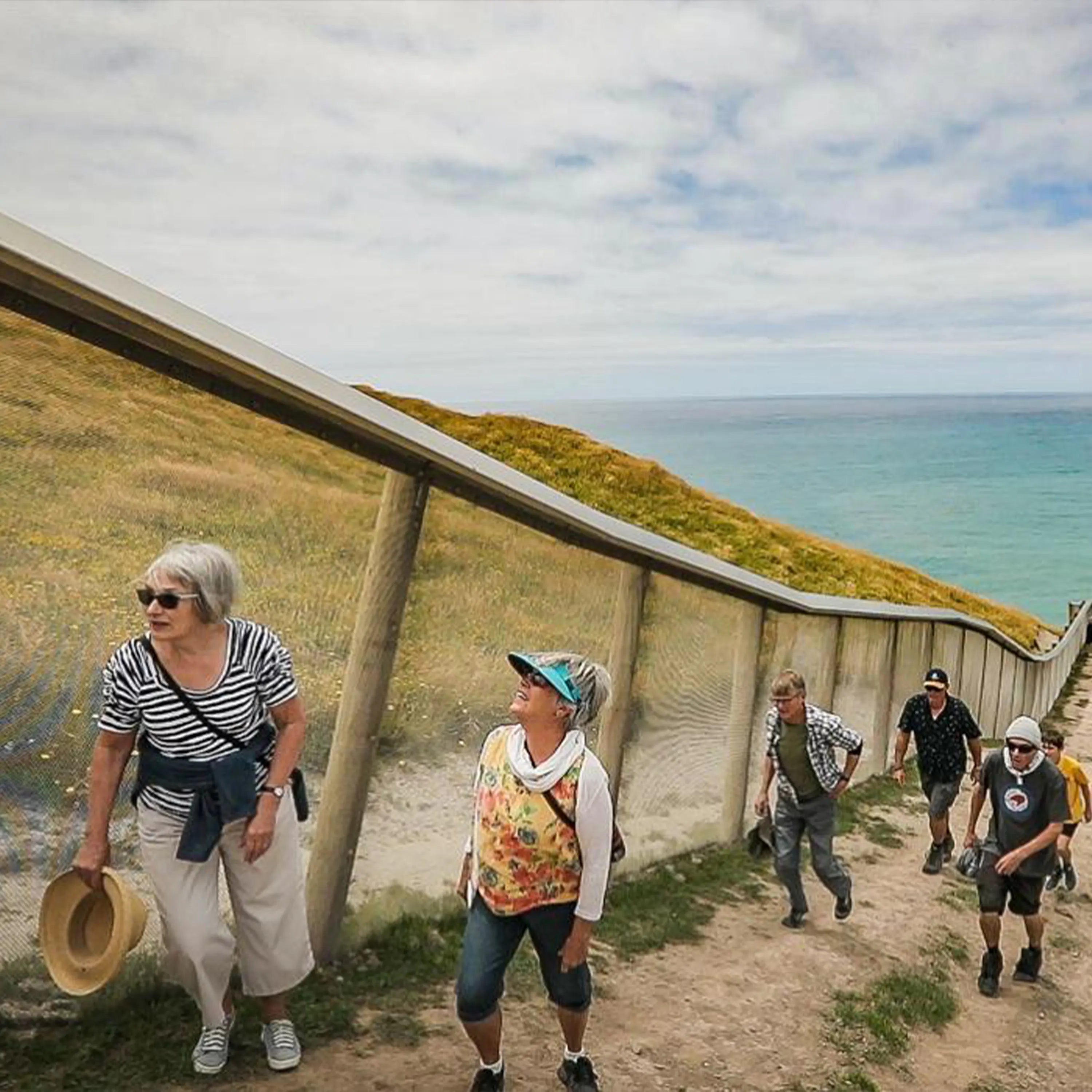 Group of people walking along a coastal path with ocean and sky in the background