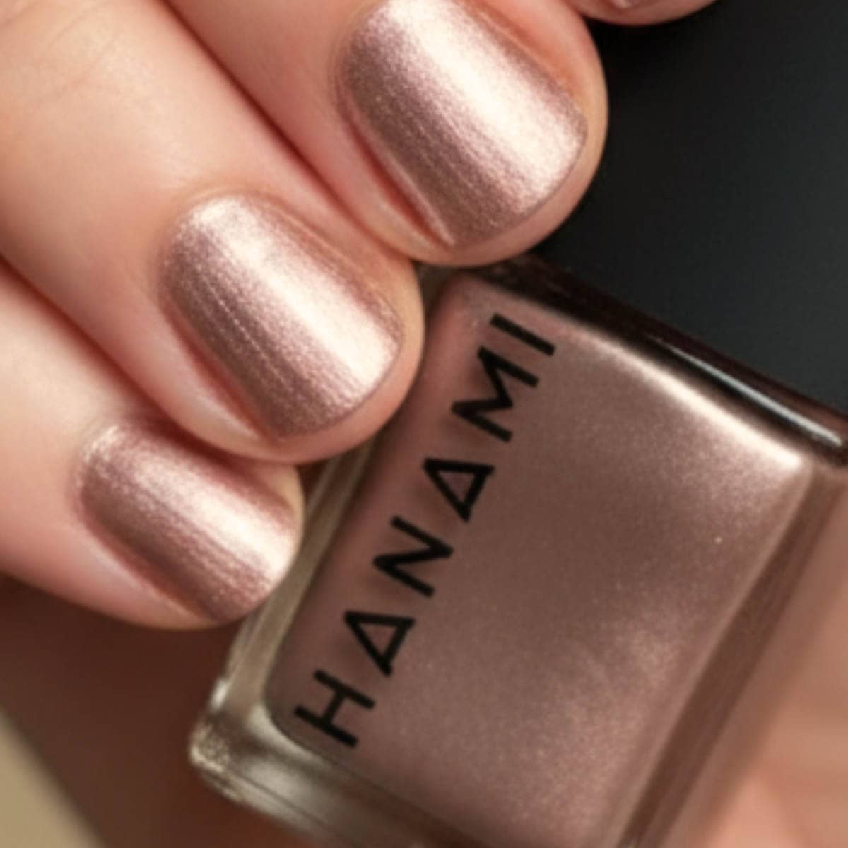 Close-up of a hand with pink nail polish holding a Hanami nail polish bottle.