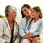 Three generations of women sitting together and smiling outdoors.