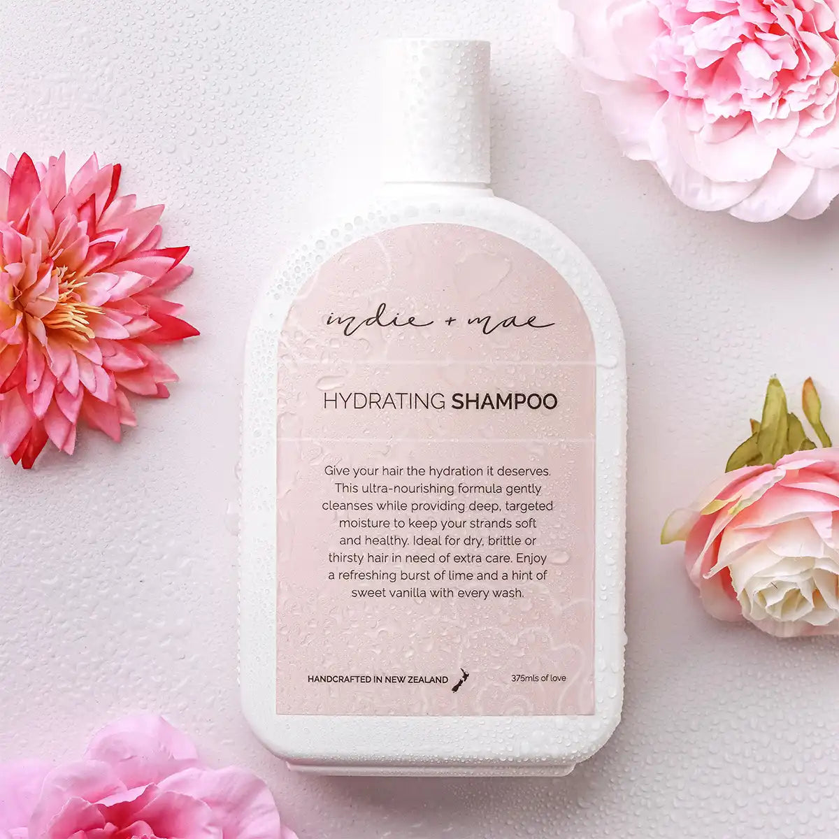 Indie + Mae hydrating shampoo bottle with pink flowers on a light background.