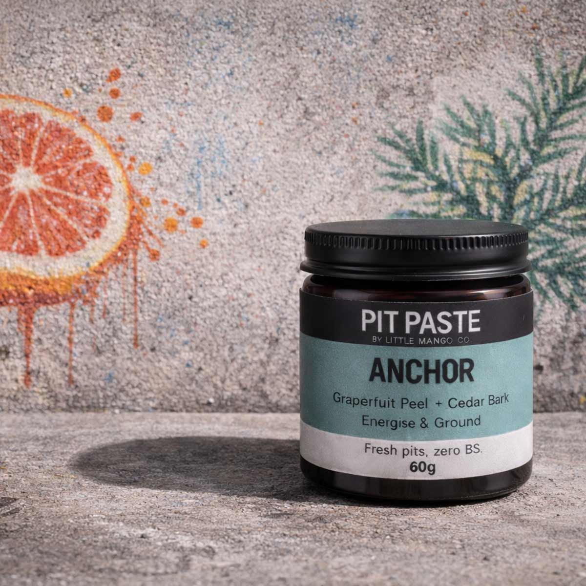 Jar of Pit Paste with on a textured surface with orange and cedar twig illustration in the background.