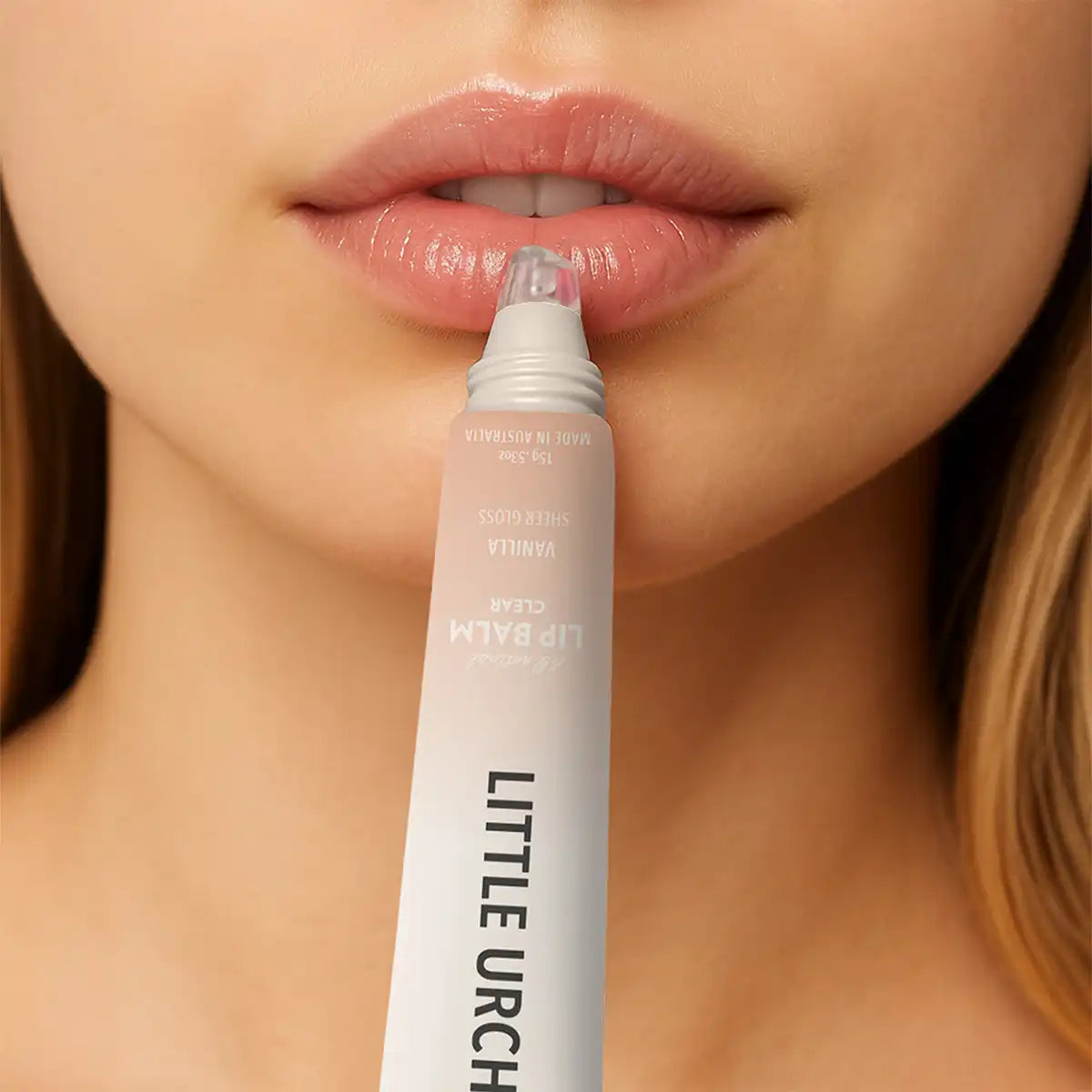 Close-up of a person applying a clear lip balm from a white tube to their lips.
