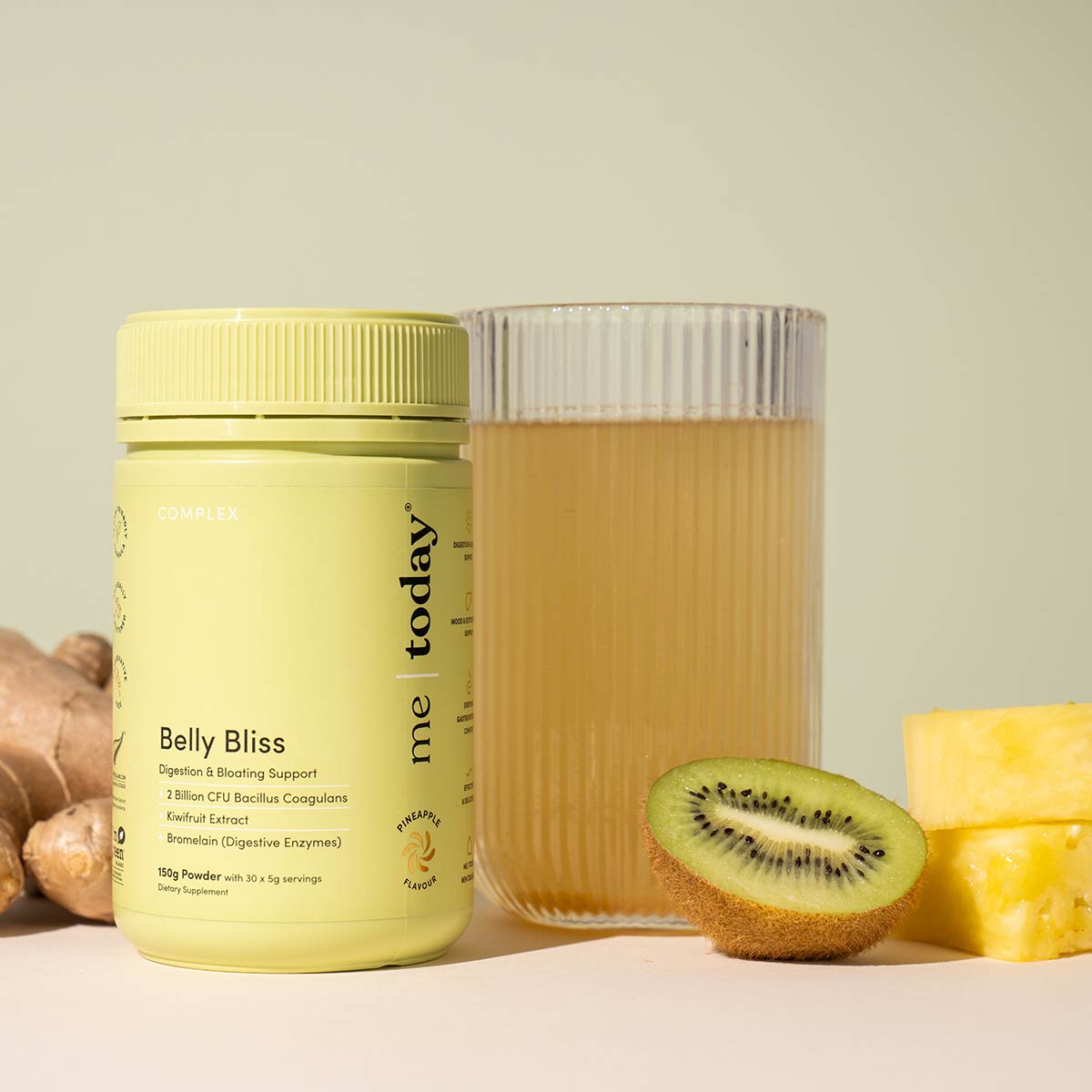 Yellow supplement bottle labeled 'Belly Bliss' next to a glass of juice and fruits on a light background