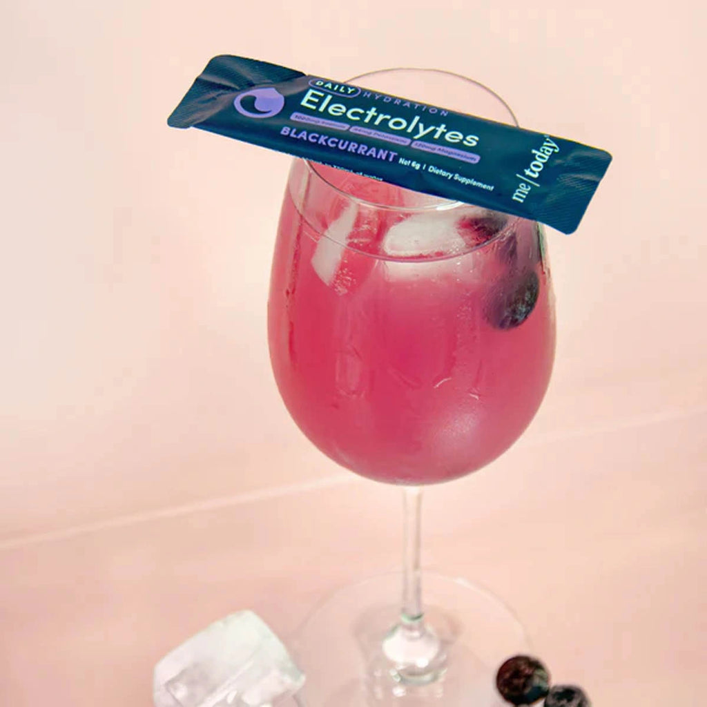 Wine glass with chilled pink blackcurrant electrolytes with sachet balanced on top.