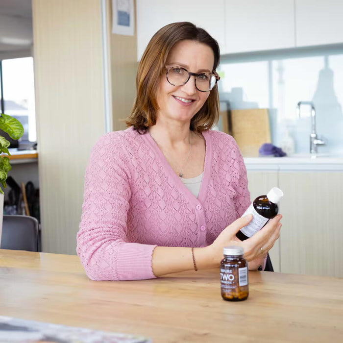HealthPost naturopath, Rebecca, holding a bottle of supplements in a kitchen setting.