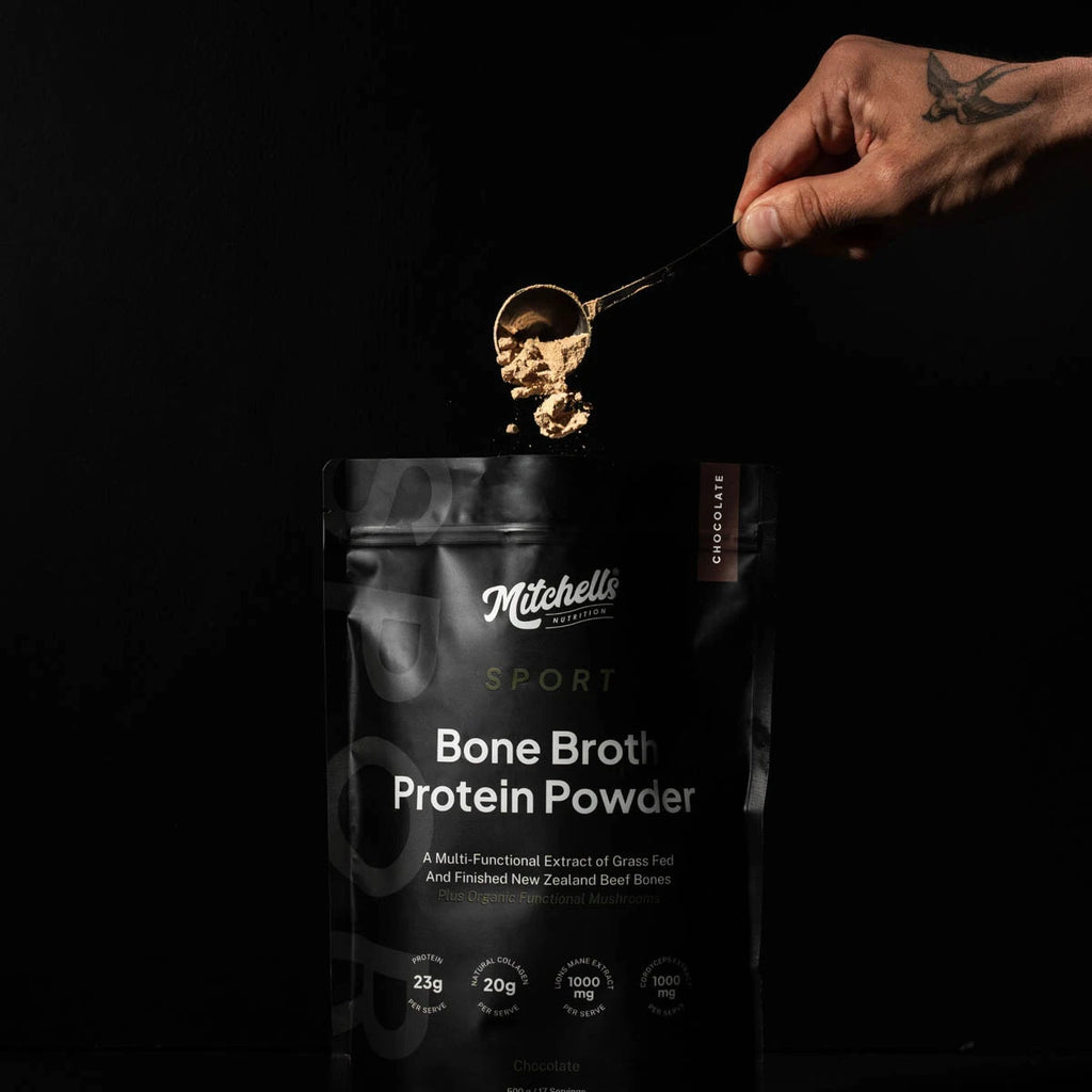 Hand scooping Mitchell's Bone Broth Protein Powder from a package against a black background